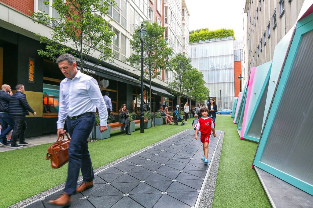 Man and child walk on Pavegen floor tiles, generating energy in an outdoor area